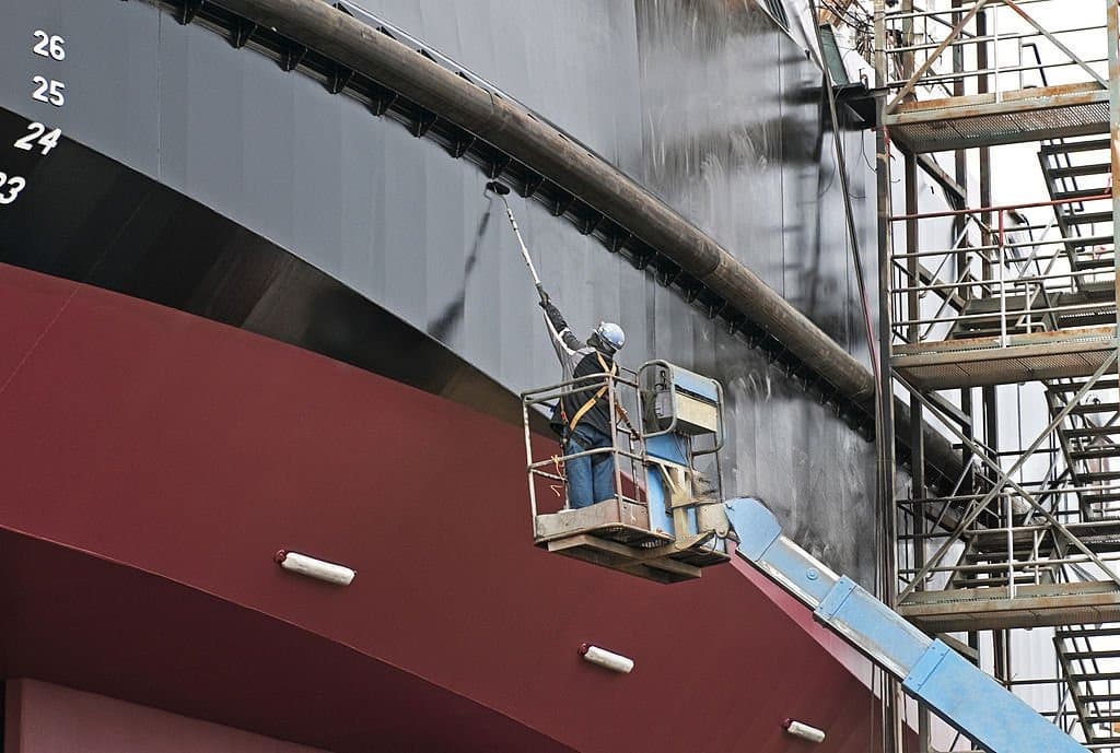Man painting ship with copper-based paint in dry dock